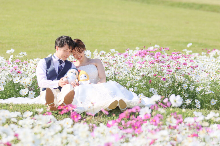 コスモス畑に座り、お気に入りのぬいぐるみを抱える新郎新婦